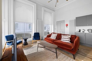 Ein modernes Wohnzimmer mit einer Couch, Sesseln, einem Couchtisch und einem Fernseher.