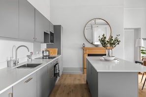 Eine moderne Küche mit grauen Schränken, einer weißen Arbeitsplatte und einem Holztisch.