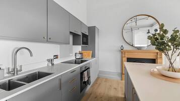 A modern kitchen with grey cabinets, a stainless steel sink, and a wooden dining table with a vase of green plants.