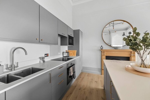 A modern kitchen with grey cabinets, a stainless steel sink, and a wooden dining table with a vase of green plants.