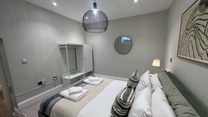 A modern bedroom with a large bed, a bedside table, a mirror, and a hanging light fixture. - Martello By Pureserviced (Plymouth)