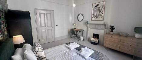 A hotel room with a bed, bedside table, lamp, dresser, and a fireplace.