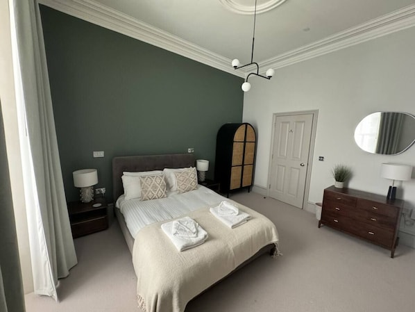 Une chambre à coucher avec un lit, des tables de chevet, une commode, un miroir et une porte.