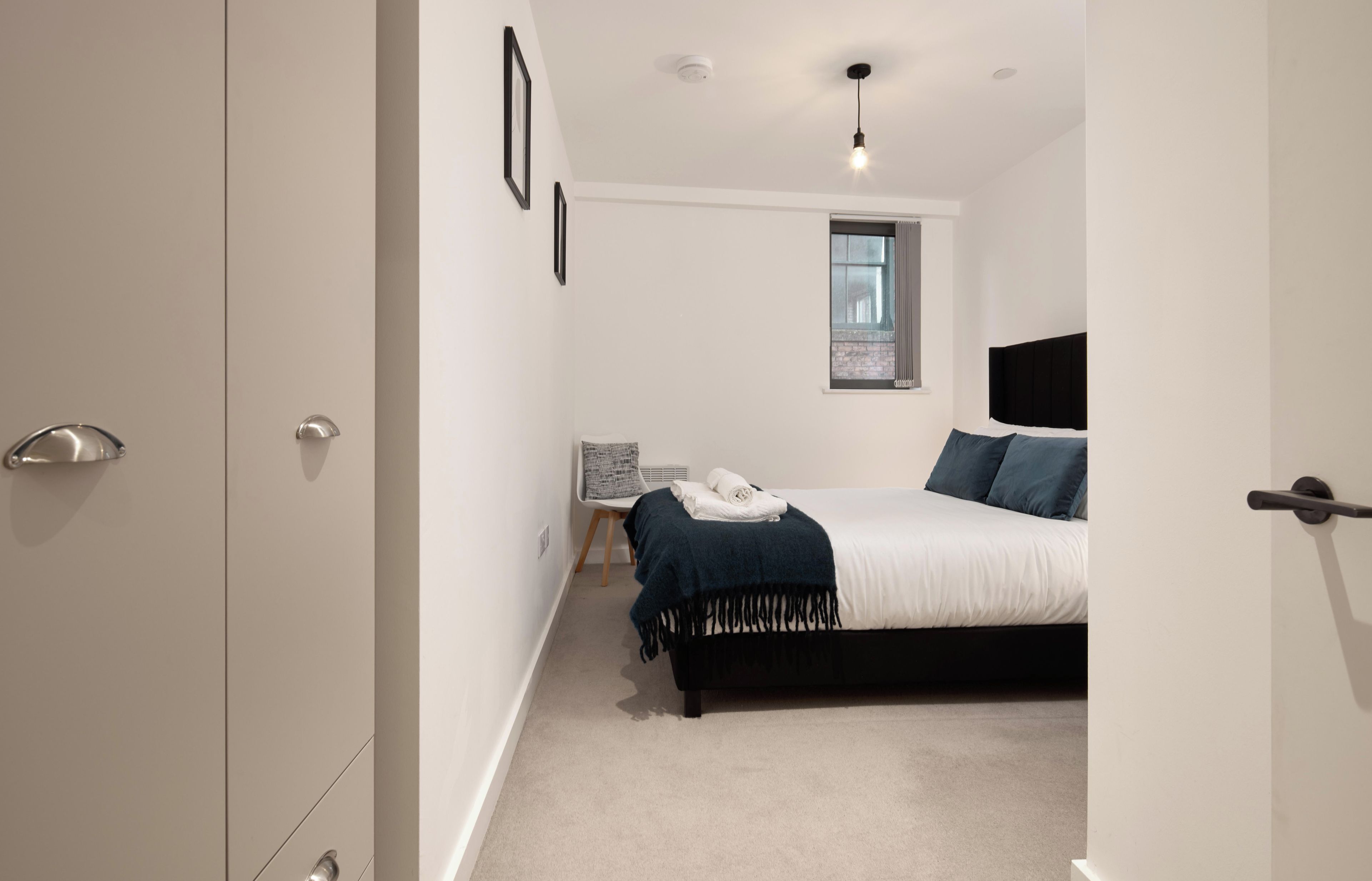 Un dormitorio con una cama, una mesita de noche, una silla y una ventana.