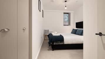 Un dormitorio con una cama, una mesita de noche, una silla y una ventana.