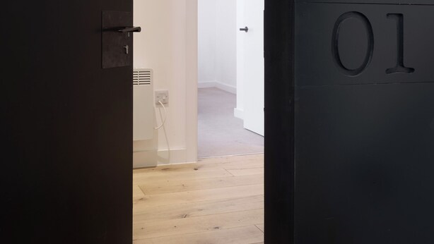 Un umbral que da a una habitación con piso de madera y una puerta blanca con un número.