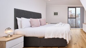 Un dormitorio moderno con una cama grande, una mesita de noche con lámpara y vistas a la ciudad a través de un ventanal.