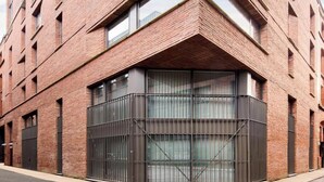 Un edificio moderno con fachada de ladrillo, ventanas grandes y una entrada destacada en la esquina.