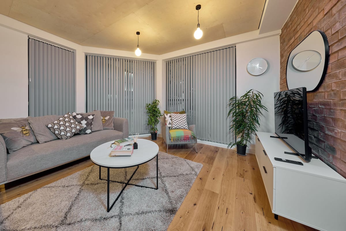 A modern living room with a grey sofa, a round coffee table, and a TV on a white cabinet.