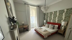 A bedroom with a bed, bedside tables, a desk, a chair, and a window with curtains. - Ranelagh By Pureserviced (Plymouth)