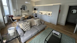 A modern living room with a sofa, coffee table, and a dining area with chairs and a table. - Ranelagh By Pureserviced (Plymouth)