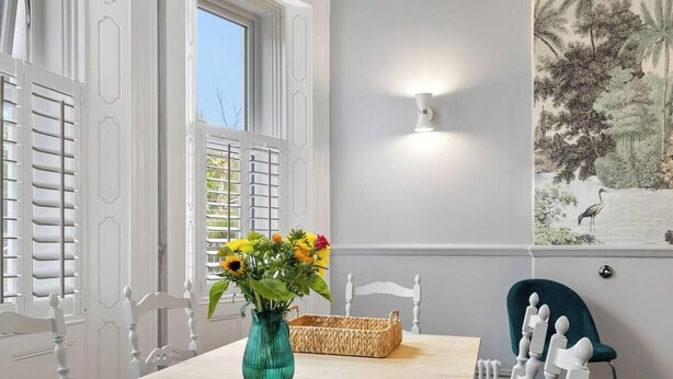 A room with a dining table, a vase with flowers, a wall-mounted light, and a mural. - Huge spacious 8 bed luxury villa (Plymouth)