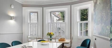 Comedor con una mesa blanca, sillas color turquesa y vistas a través de un ventanal.