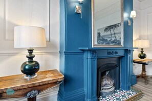 A room with a blue fireplace, a wooden side table with a lamp, and a patterned rug.