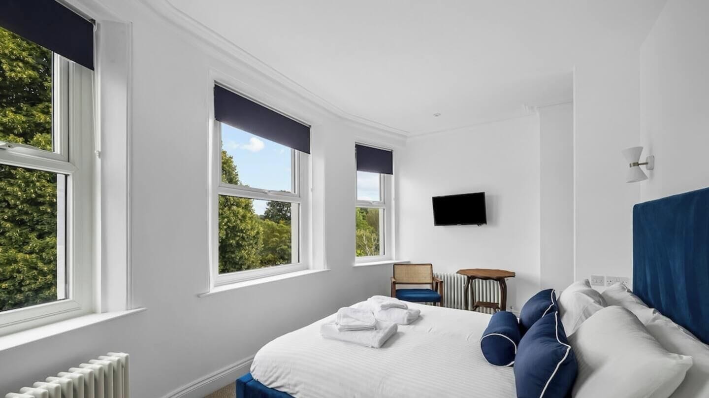A hotel room with a large bed, a television, and a view of greenery outside.