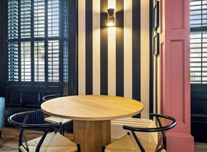 A round wooden table with four chairs, positioned in front of a wall with vertical black and white stripes.