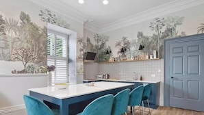 A kitchen with a central island, bar stools, a window with blinds, and a door. - Huge spacious 8 bed luxury villa (Plymouth)