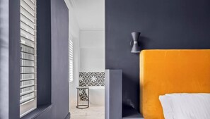 Une chambre moderne avec une grande fenêtre, un mur noir, une tête de lit jaune et un oreiller blanc.