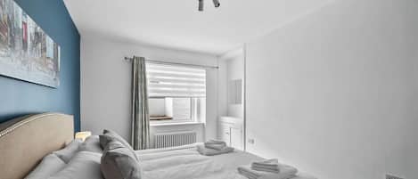 A hotel room with a bed, a window with blinds, a radiator, and a ceiling light.