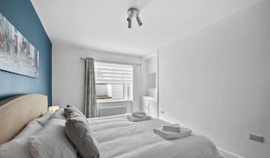 Una habitación de hotel con cama, ventana con persianas, radiador y luz en el techo.