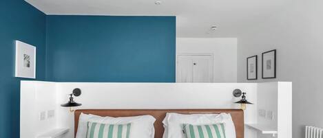 A bedroom with a bed, two bedside lamps, a white headboard, and a blue accent wall.