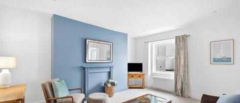 Una sala de estar con una pared azul decorativa, una chimenea, un televisor y una ventana con cortinas.