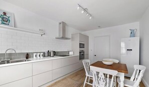 A modern kitchen with white cabinetry, a stainless steel sink, and a wooden dining table with white chairs.