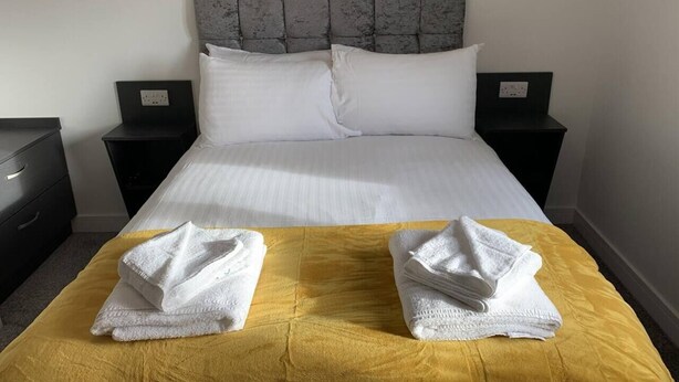 A hotel room with a bed, two nightstands, a dresser, and towels on the bed. - Paddington by Pureserviced Deluxe Family Room (Plymouth)