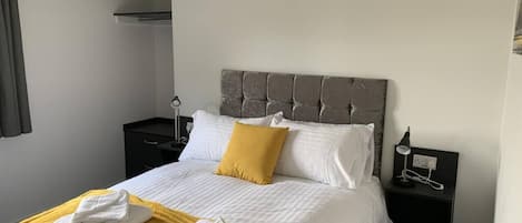 Una habitación de hotel con cama, mesita de noche, lámpara y una toalla sobre la cama.