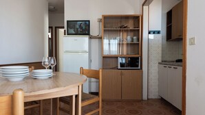 A compact kitchen with a dining table, chairs, a microwave, and a refrigerator. - Cozy Apartment Near the Beach in Bibione (San Michele al Tagliamento)