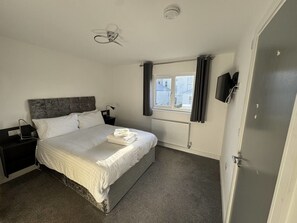 A bedroom with a bed, a nightstand, a ceiling fan, a window with curtains, a radiator, and a door. - Paddington by Pureserviced Superior Rooms (Plymouth)