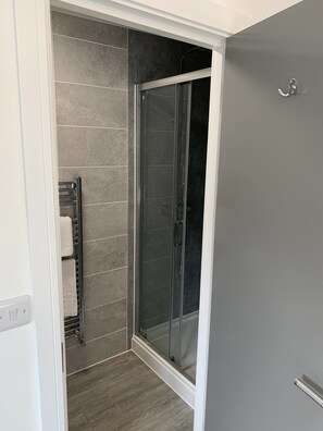A modern bathroom with a glass shower enclosure, grey tiles, and a towel rack. - Paddington by Pureserviced Superior Rooms (Plymouth)