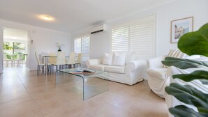 A modern living room with a glass coffee table, white furniture, and large windows with blinds. - Seatown - Spacious Townhouse Close to Pippi Beach & Yamba Shops - Holiday Yamba (Yamba)