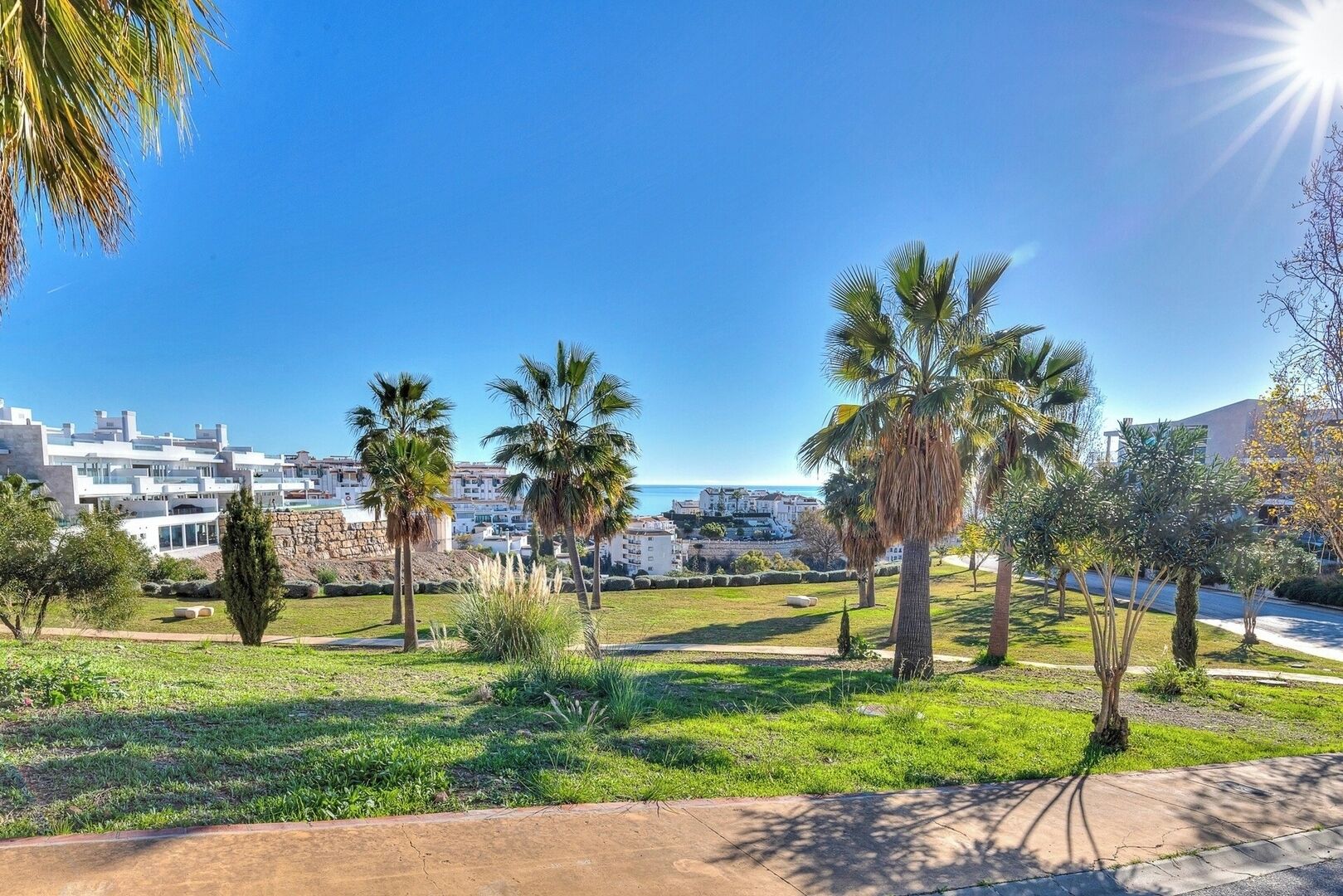 A coastal residential area with modern buildings, palm trees, and a clear blue sky.