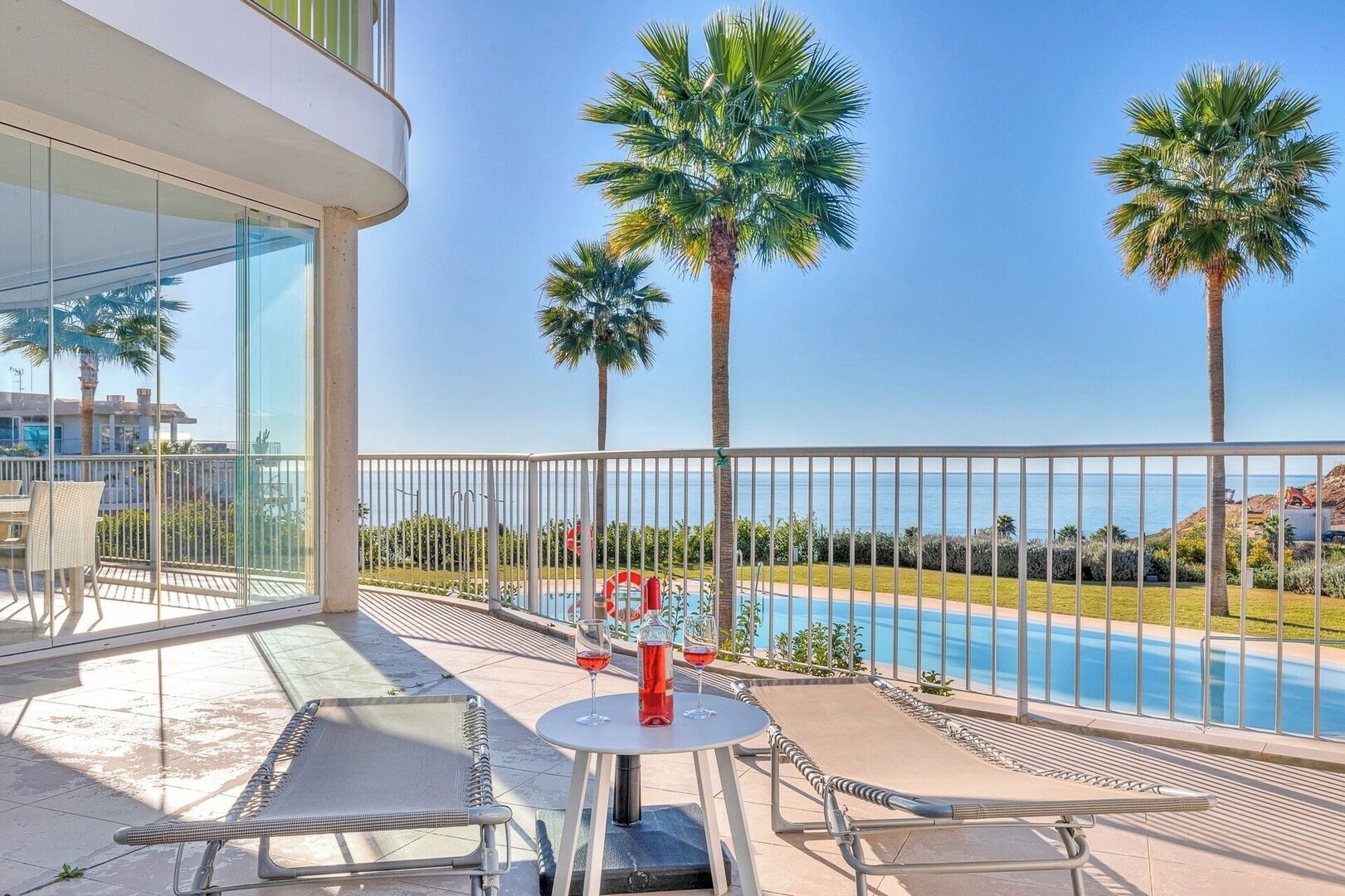 Ein Balkon mit Pool, Palmen und einem Tisch mit Flasche und Glas.
