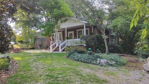 Ein Haus mit Veranda, einer Treppe und einem Garten mit Hecke und kleinem Baum.