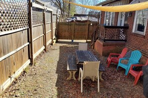 Ein Garten mit einem Holztisch, Stühlen, einem Holzzaun und einem Ziegelhaus.