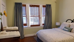 Ein Schlafzimmer mit Bett, Nachttisch, Lampe und einem Fenster mit Vorhängen.