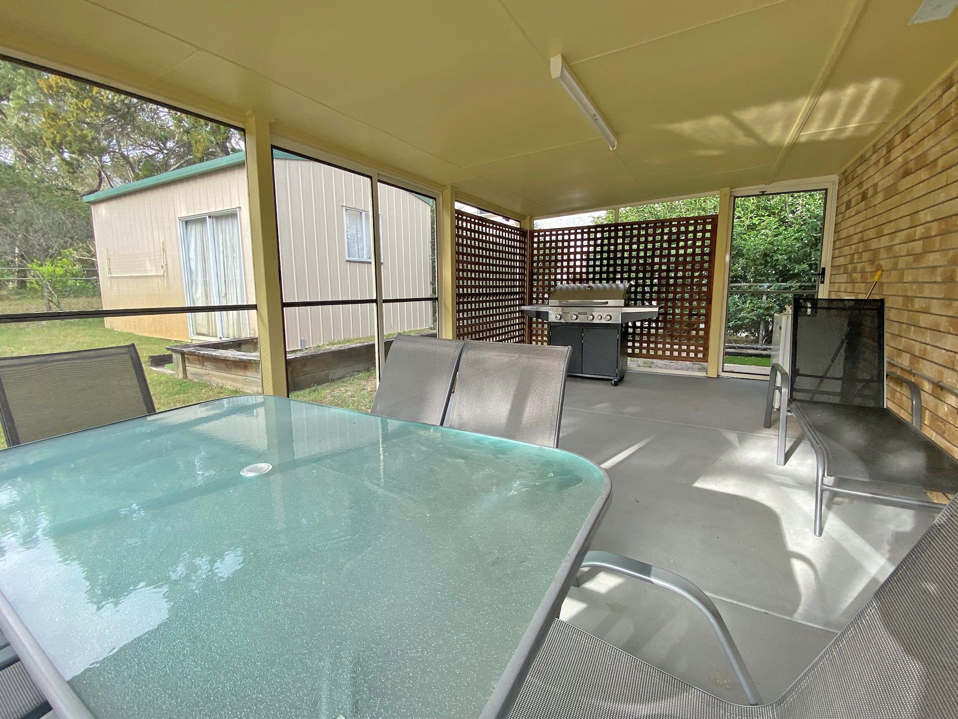 Une terrasse couverte avec une table et des chaises en verre, un barbecue et une vue sur le jardin arrière.