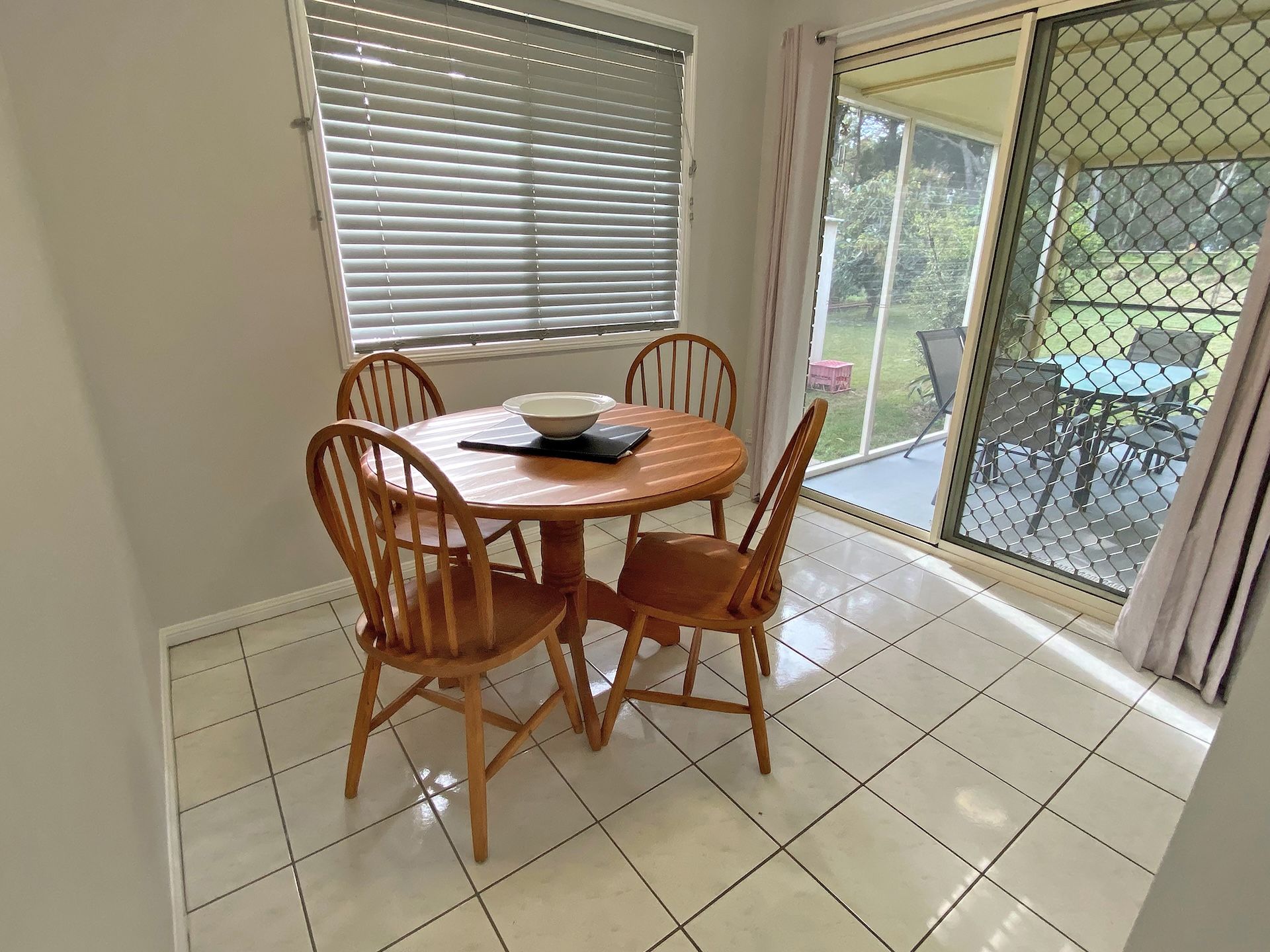 Un coin repas avec une table ronde en bois et quatre chaises, un bol et une télécommande posés sur la table.