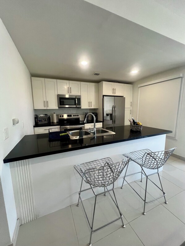 A modern kitchen with white cabinets, stainless steel appliances, a black countertop, and two bar stools.