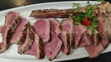 Een bord met plakjes steak, gegarneerd met peterselie en een kerstomaat.