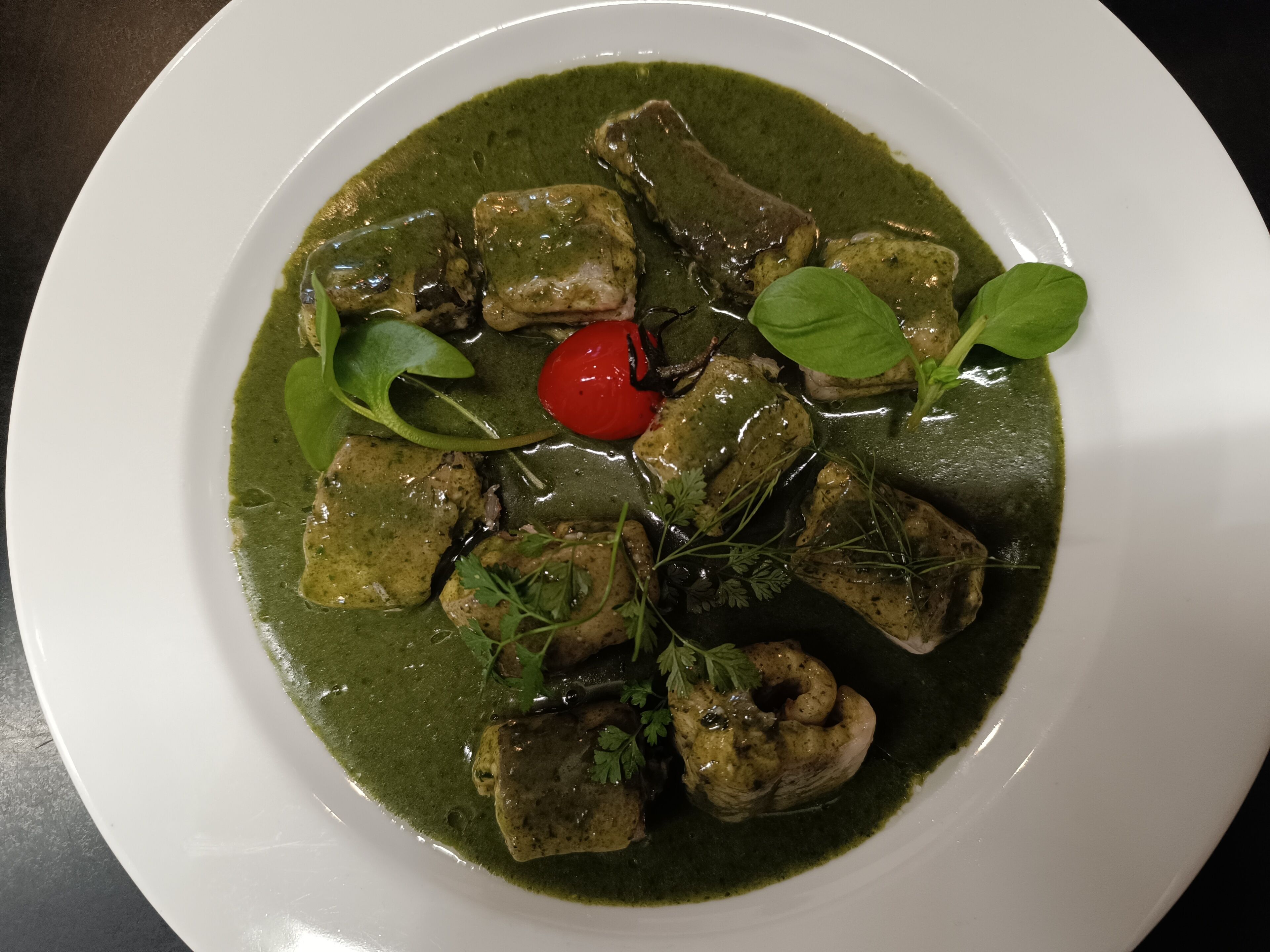 Un plato de comida con salsa verde, carne y un tomate cherry.