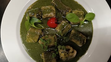 A plate of food with green sauce, meat, and a cherry tomato.