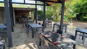 An outdoor patio with tables and chairs, a covered seating area, and a view of the surrounding greenery. - ' t Bed en tafel (Avelgem)