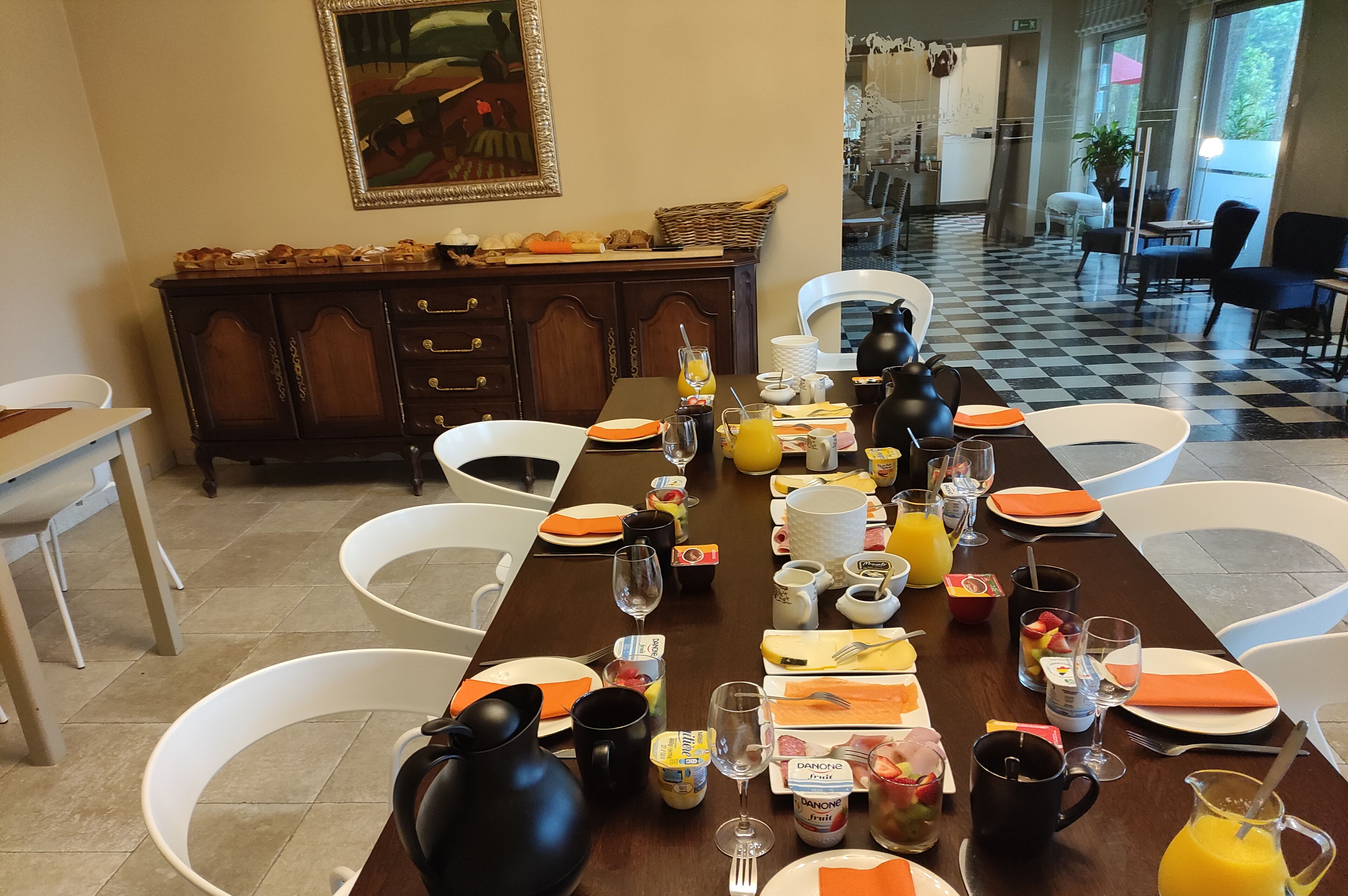 A dining area with a long table set for breakfast, including plates, cutlery, glasses, and various food items.