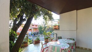 A covered outdoor patio with a table and chairs, surrounded by potted plants and trees. - Holiday apartment mit Klimaanlage und Terrasse (Pješćana Uvala)