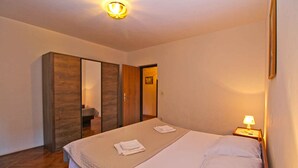 A hotel room with a bed, a bedside lamp, a wooden wardrobe, and a door leading to another room. - Holiday apartment mit Klimaanlage und Terrasse (Pješćana Uvala)