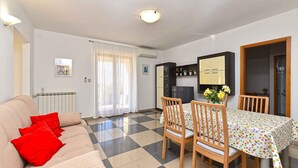 A dining area with a checkered floor, a table with a polka dot tablecloth, and wooden chairs. There is a sofa with red cushions and a radiator in the background. - Holiday apartment mit Klimaanlage und Terrasse (Presika)