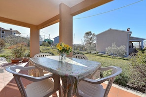 Une terrasse avec une table et des chaises, un vase rempli de fleurs et une vue sur un quartier résidentiel avec des maisons et des arbres.